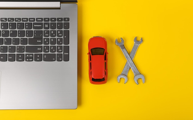 Foto laptop com carro de brinquedo e chaves em um fundo amarelo centro de serviço de diagnóstico on-line oficina de reparação de automóveis vista superior