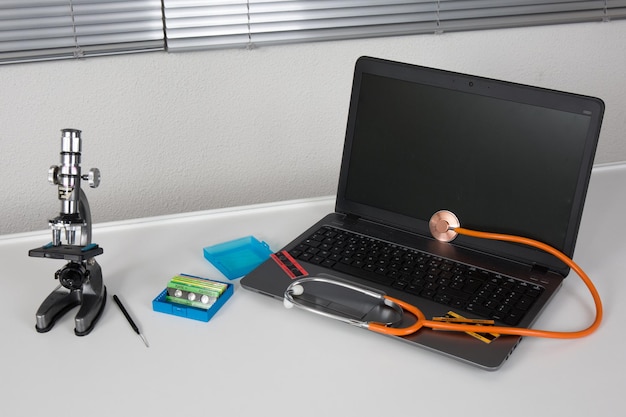 Foto laptop com estetoscópio laranja no fundo cinza