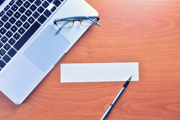 Laptop com etiqueta em branco e caneta na mesa de madeira