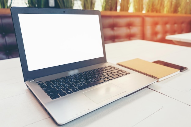 Laptop com notebook de tela branca em branco e telefone inteligente em cima da mesa no caderno da sala de escritório no café