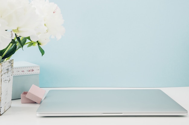 Laptop com tela em branco branca e flores em um vaso na mesa em azul. brincar