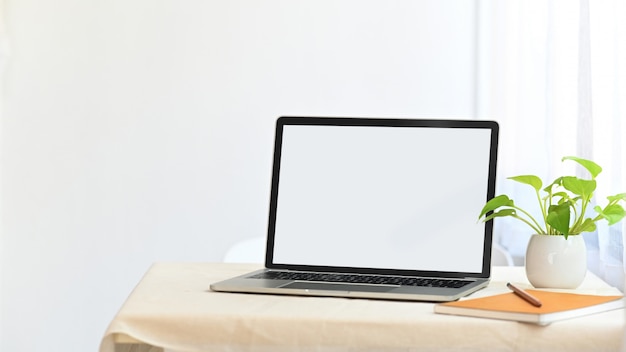 Laptop com tela em branco branca, juntando plantas em vaso, caderno e lápis na mesa moderna, com confortável sala de estar como