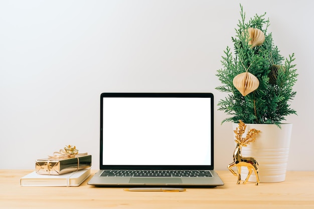 Laptop com tela em branco de maquete em uma mesa de madeira com árvore de abeto de presente de Natal em fundo branco