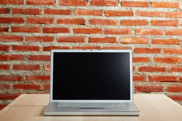 Laptop com tela em branco na mesa e parede de tijolo vermelho funciona em casa ou estudo online