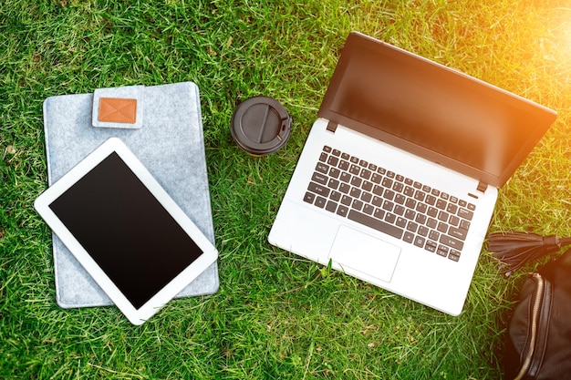 Laptop-Computer auf grünem Gras mit Kaffeetassenbeutel und Tablet im Park im Freien