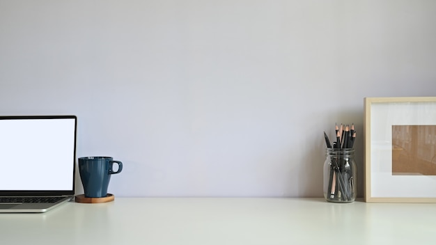 Laptop-Computer, Kaffee, Bleistift und Fotorahmen auf Arbeitsplatz.