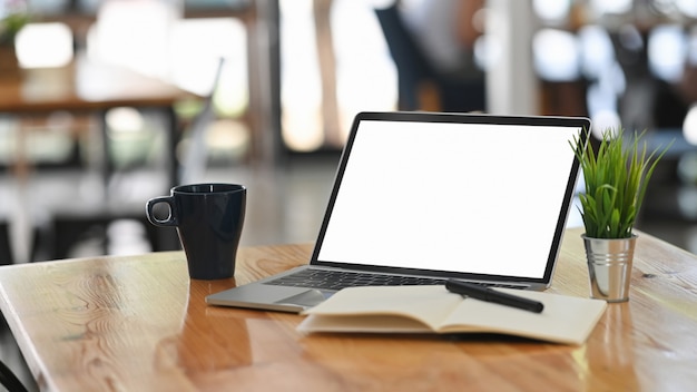 Laptop-Computer, Kaffee, Notizbuch und Stift auf Holztisch auf Co-Arbeitshintergrund.