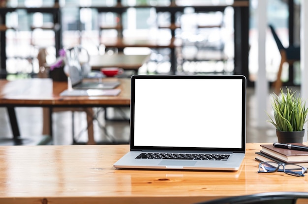 Laptop-Computer mit leerem Bildschirm und Zubehör auf Holztisch im modernen Büroraum mit Kopienraum.