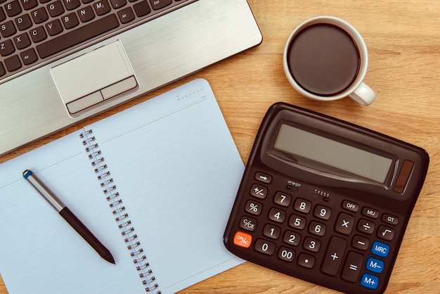 Laptop-Computer oder Notizbuch, Taschenrechner und Tasse Kaffee auf Tabelle