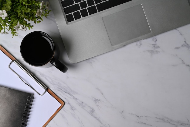 Laptop-Computer, Tasse Kaffee, Zimmerpflanze und Zwischenablage auf Marmorhintergrund.