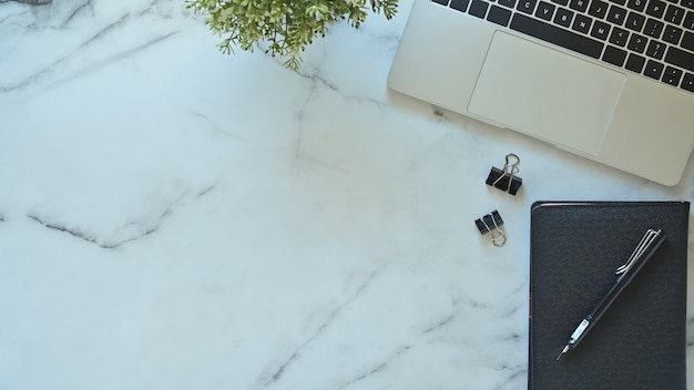 Laptop de mesa de escritório, caneta e caderno com planta na mesa de mármore com vista superior