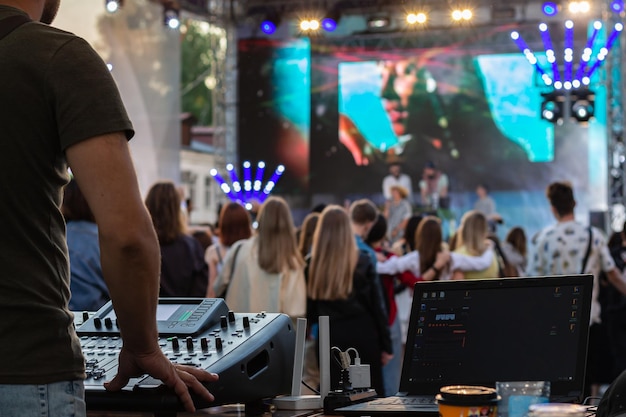 Laptop de misturador de música DJ profissional de baixa luz no festival de festas com multidão de pessoas em segundo plano