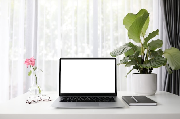 Laptop de mock-up com planta rosa e calathea orbifolia e notebook na mesa de madeira branca