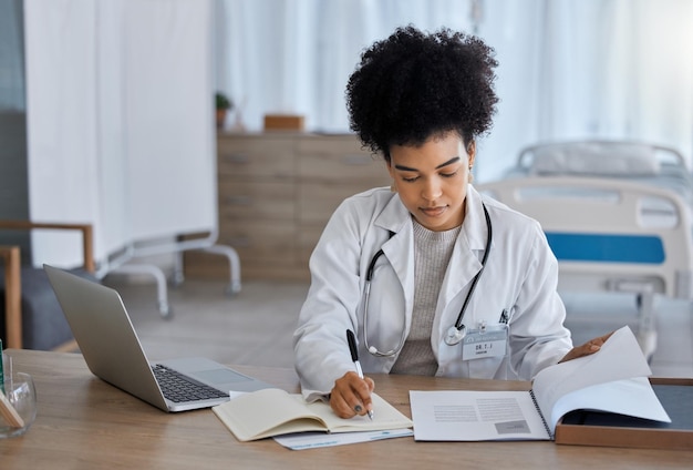 Laptop de mulher negra e médico escrevendo em caderno para estudo ou pesquisa de teste de saúde no hospital Especialista em medicina afro-americana fazendo anotações em livro para relatório ou resultados de seguro