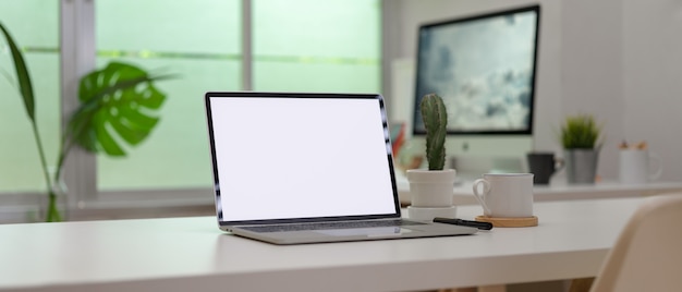 Laptop de tela em branco em uma mesa branca com material de escritório em uma sala de escritório moderna