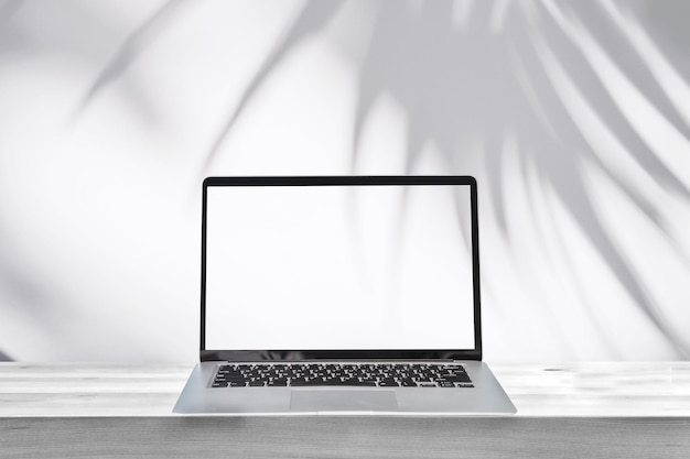 Laptop de tela vazia em uma mesa de madeira com sombra de folha de palmeira em fundo de parede de cimento branco e espaço de cópia