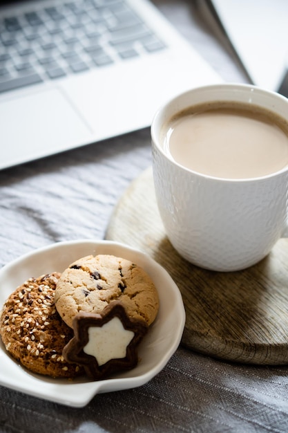Laptop de trabalho em casa real com xícara de café com biscoitos na cama com cobertor aconchegante