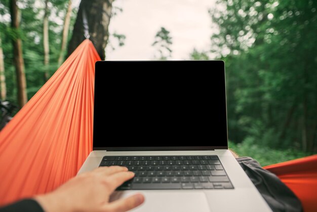 Foto laptop de um nômade digital remoto em uma rede com a primeira perspectiva de fundo de floresta verde trabalhando em um laptop moderno enquanto está na natureza