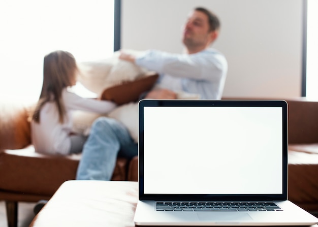 Laptop delante de hija y padre jugando con almohadas