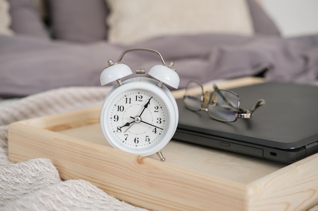 Laptop, despertador e óculos em uma bandeja na cama do quarto. Hora de trabalhar.