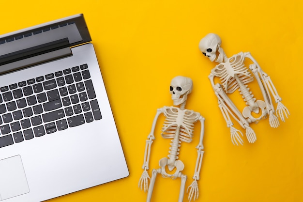 Laptop e esqueletos em um fundo amarelo. Vista do topo