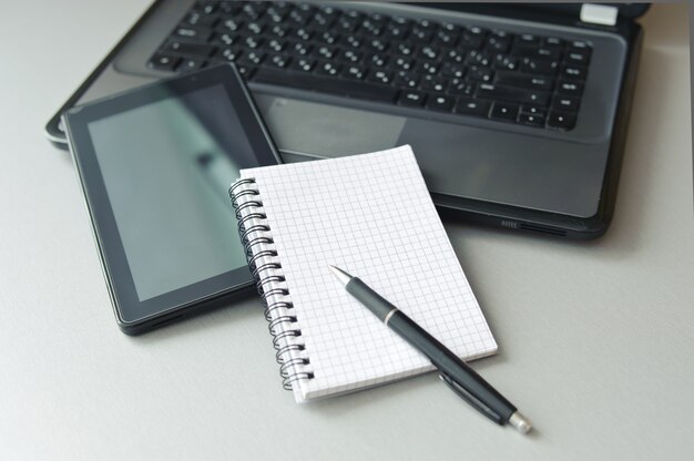 Laptop e tablet perto de caderno e caneta em cima da mesa