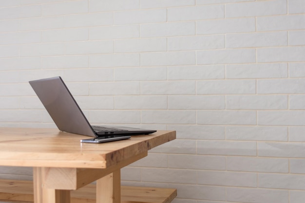 Laptop e telefone na mesa de madeira com parede de tijolos brancos no fundo