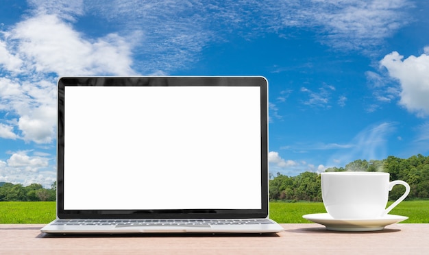 Laptop e xícara de café na mesa vista do agente da grama verde agente de campo céu azul no campo