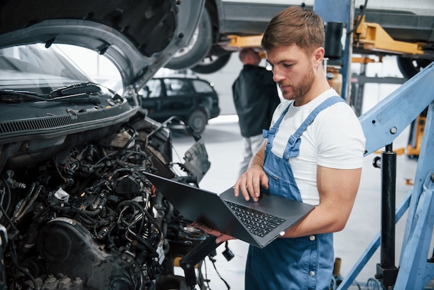 Con laptop. Empleado en el uniforme de color azul trabaja en el salón del automóvil