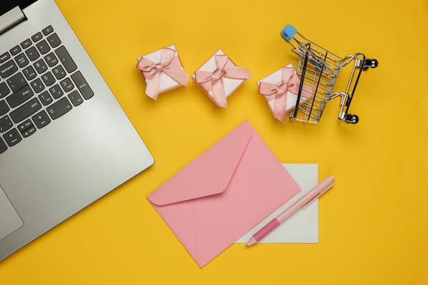 Laptop, envelope com carta e caneta, caixas de presentes e carrinho de compras em fundo amarelo. natal, dia dos namorados, aniversário. vista do topo