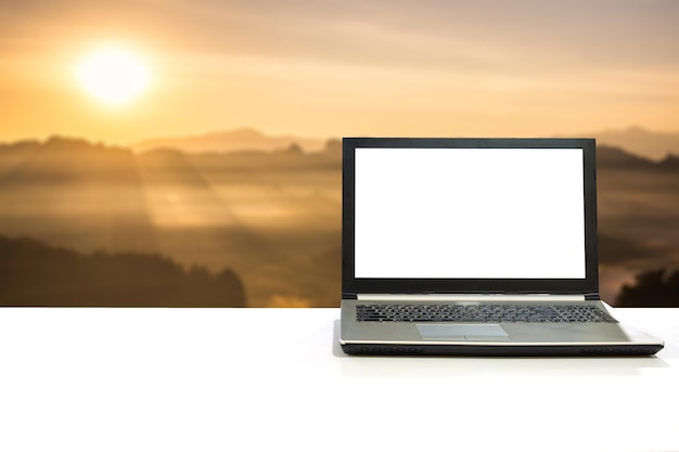 Laptop en escritorio blanco con luz de sol de escena borrosa brillando en la montaña al amanecer