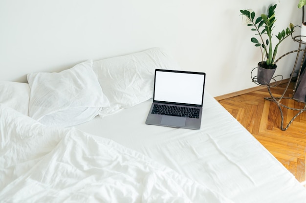 Laptop con espacio de copia pantalla vacía en la cama con sábanas blancas