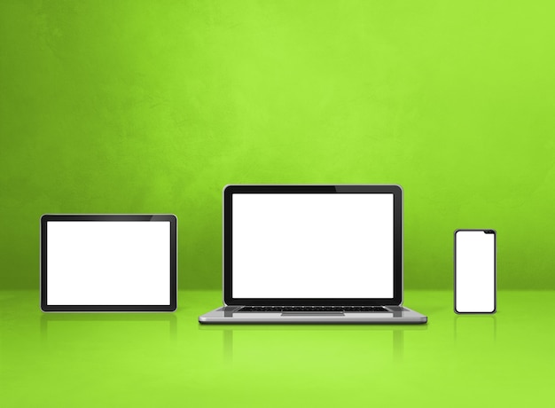 Laptop, Handy und digitaler Tablet-PC auf grünem Schreibtisch.