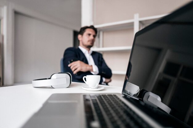 Laptop, Kopfhörer, Kaffeetasse und Geschäftsmann im Hintergrund