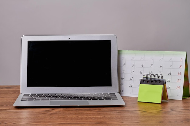 Laptop macbook com calendário e notas adesivas no notebook de mesa de madeira com tela preta para cópia