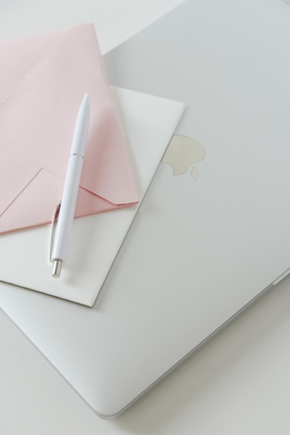Laptop Macbook Pro com envelopes brancos e rosa e uma caneta branca