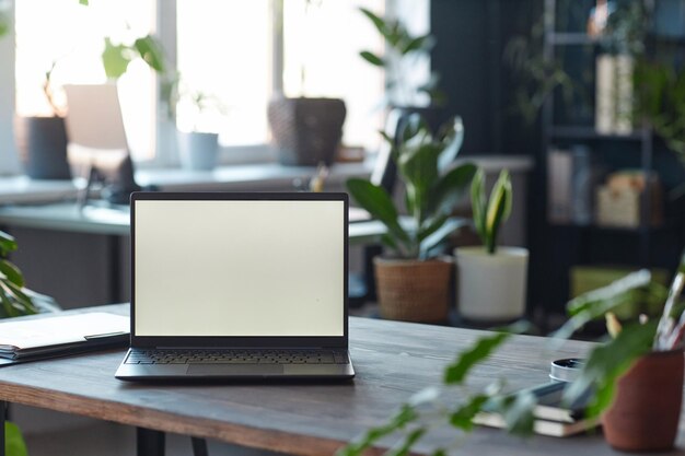 Laptop en la mesa del lugar de trabajo en la oficina con pantalla blanca en blanco
