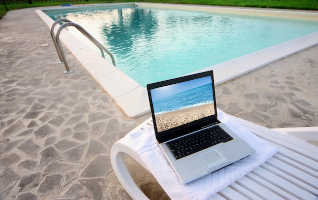 Laptop mit Bildschirmschoner am Strand entlang eines Swimmingpools