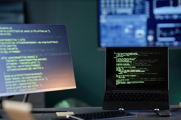 Laptop mit Code auf dem Bildschirm steht auf dem Schreibtisch des Programmierers mit Computern im Büro
