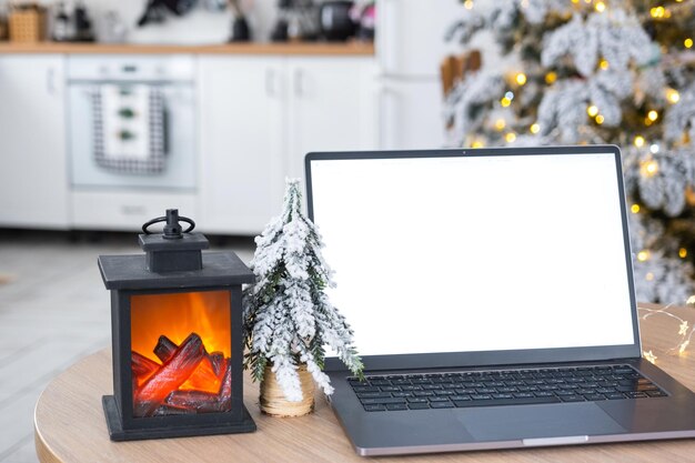 Laptop mit einem weißen Bildschirm im gemütlichen, weiß dekorierten Weihnachtsküchen mit Feenlichtern