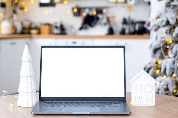 Laptop mit einem weißen Bildschirm im gemütlichen, weiß dekorierten Weihnachtsküchen mit Feenlichtern