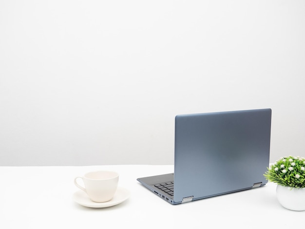 Laptop mit Kaffeetasse und Vase auf dem weißen Hintergrund des Tisches