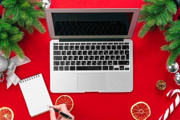 Laptop mit Pelzbaumasten und Weihnachtsdekorationen auf Draufsicht des roten Hintergrundes