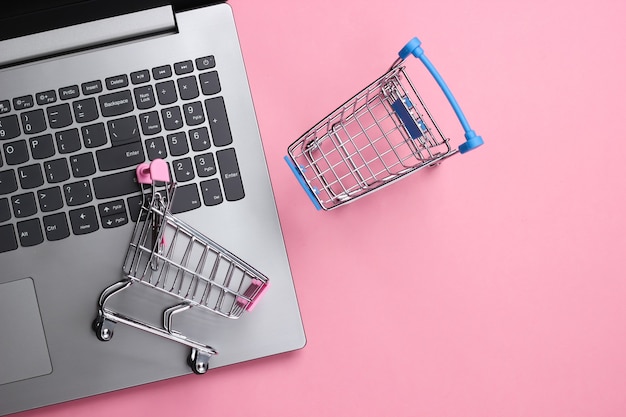 Laptop mit Supermarktwagen auf einem rosa Pastell