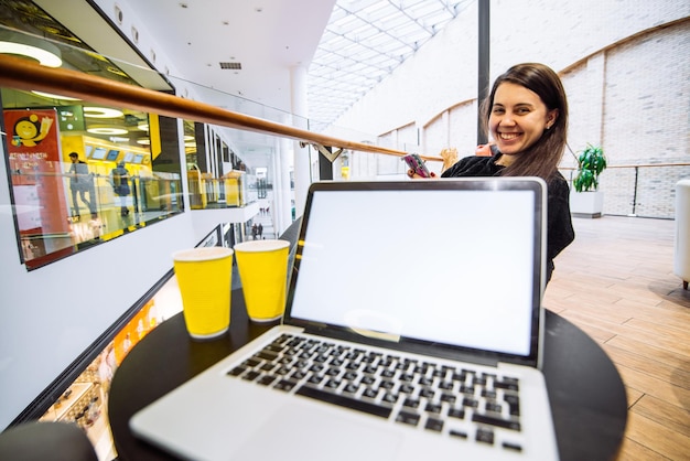 Laptop mit weißem Bildschirm im Café lächelnde Frau mit Telefon im Hintergrund Lifestyle-Konzept
