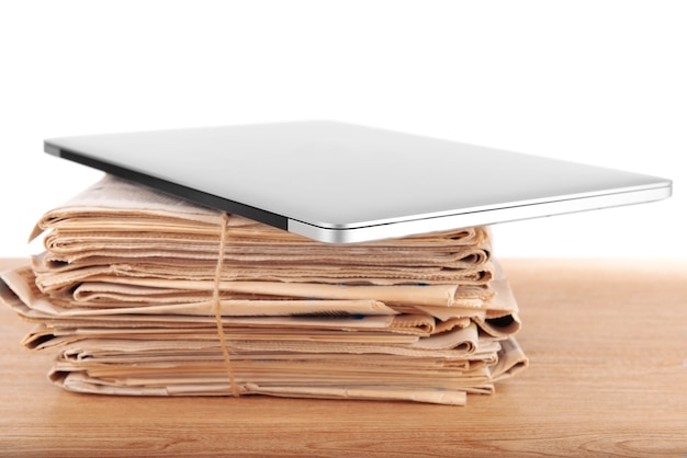 Laptop mit Zeitungsstapel auf Tisch auf weißer Fläche