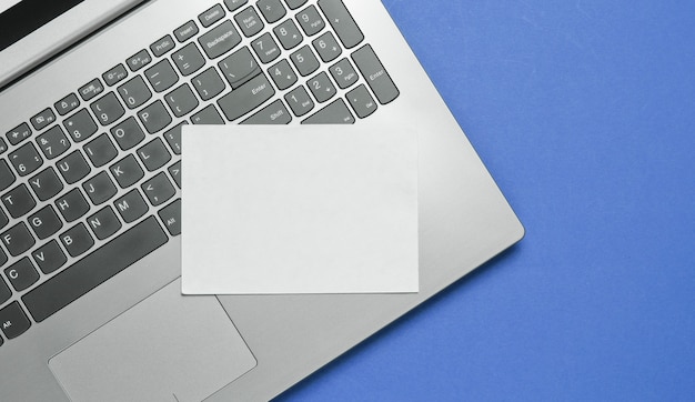 Laptop moderno e folha de papel branco para espaço de cópia sobre fundo azul. vista do topo