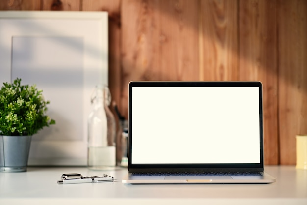 Laptop mostrando a tela em branco em uma mesa de madeira branca com um cartaz branco e acessórios