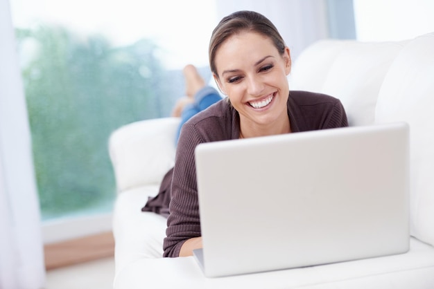 Foto laptop de mujer feliz y relajarse en el sofá para el trabajo remoto transmisión de películas y actualización de publicaciones de blog en casa computadora independiente y descarga suscripción compras en línea y búsqueda de noticias en redes sociales