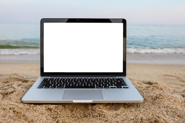 Laptop na areia na praia de verão em plano de fundo com tela branca.